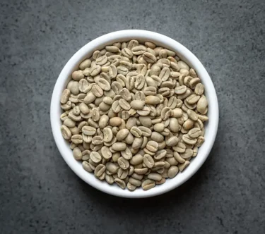 Bowl of Papua New Guinea NOP Enorga Organic green coffee beans on a dark stone background