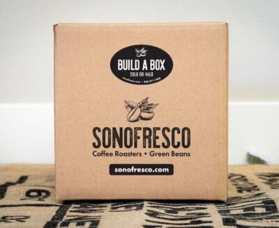 Sonofresco cardboard box labeled “Build A Box – 20lb or 46lb” on burlap sacks, used for packaging custom orders of green coffee beans.
