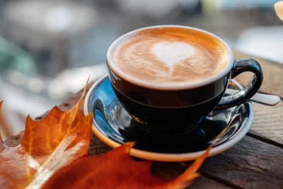 Cappuccino with latte art beside an autumn maple leaf
